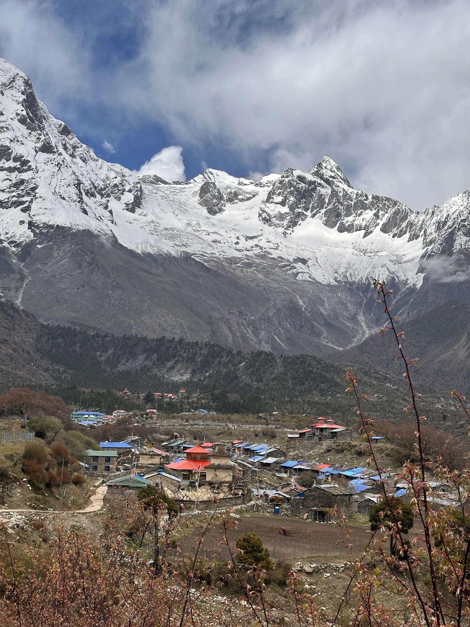 A remote mountain village with colorful roofs sits in a valley below towering, cloud-wrapped snowy peaks.
