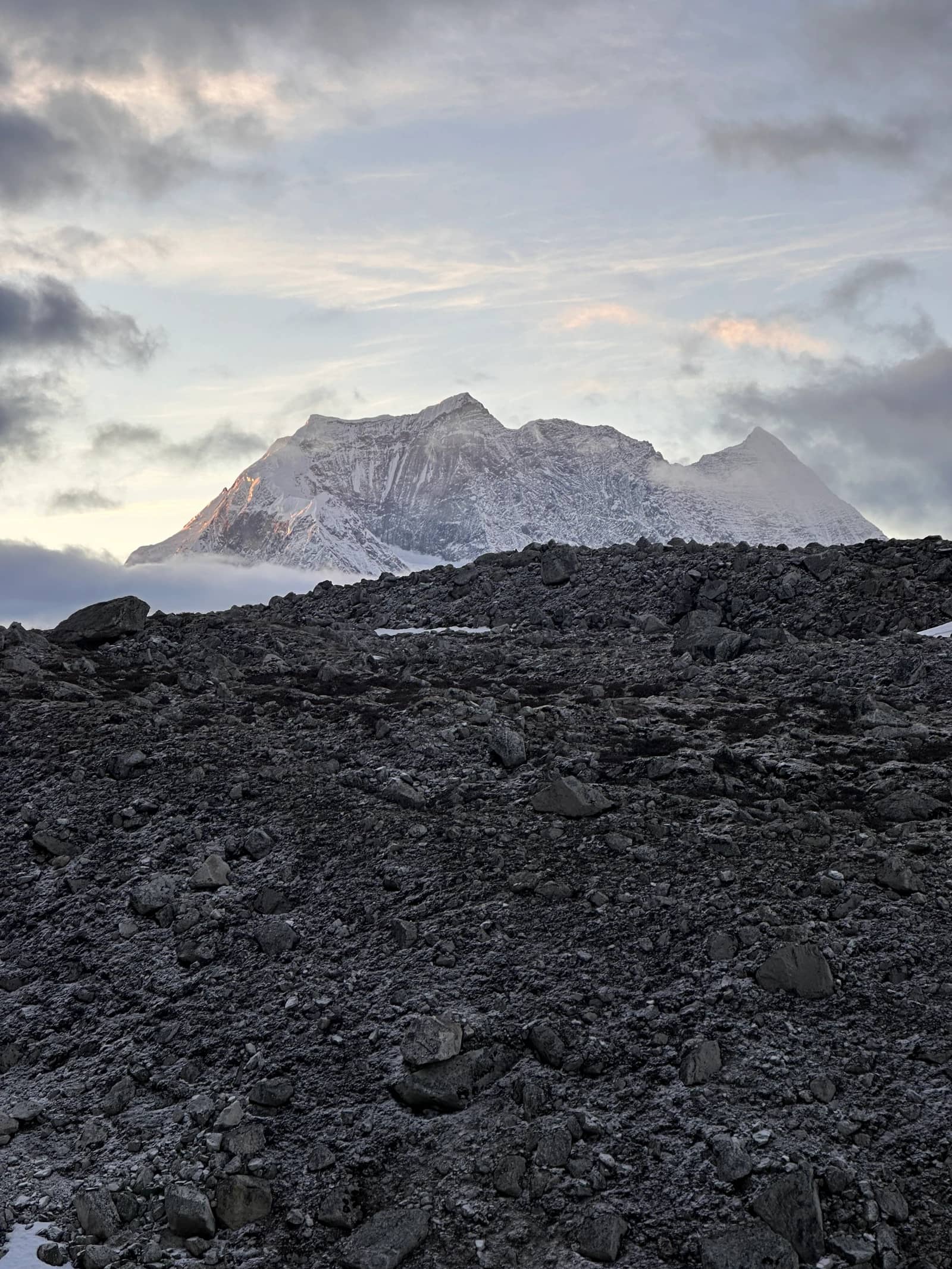 A jagged snow-capped mountain catches the first sunlight above a vast, dark, rocky scree slope.